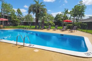 outdoor pool with fencing, patio tables with umbrella and chairs, sun loungers