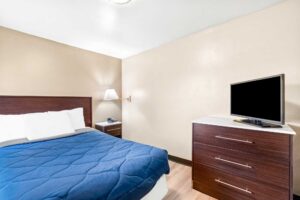 Double bed, night stand with telephone, wall bedside lamp, wooden drawer unit with TV, laminate flooring