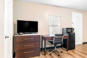 Wooden drawer unit with TV, desk with chair, fridge with microwave, laminate flooring