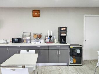 Breakfast options display counter with cereal and coffee machine, toaster oven, fridge with chilled items, milk and juice, tables and chairs, tiled flooring